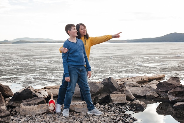 Mom and son are standing on the river bank with a Chihuahua dog. Nature and recreation.