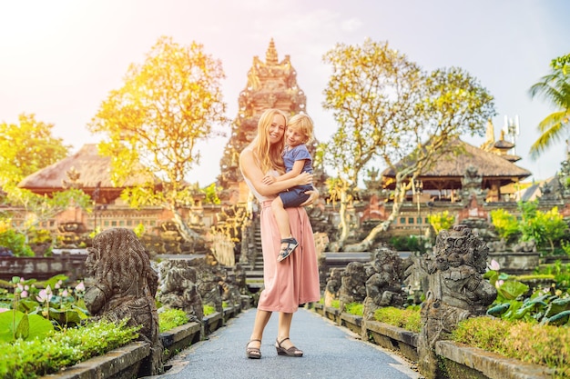 Mom and son travelers in the background of Pura Taman Kemuda Saraswati Temple in Ubud, Bali island, Indonesia Traveling with children concept with sunlight