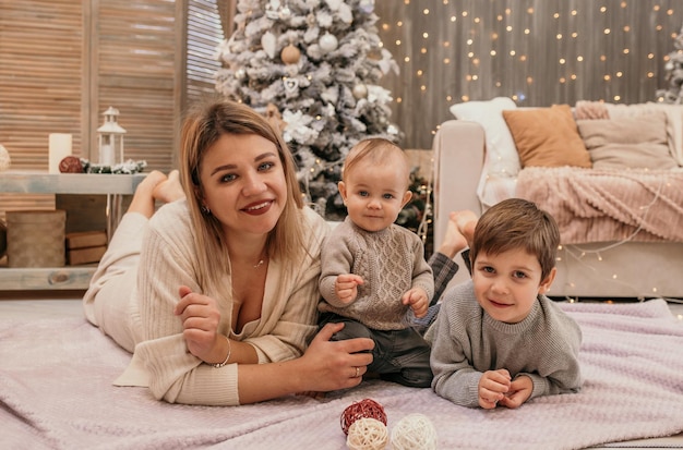 Mom and sons are lying on a blanket in the room and hugging around the Christmas tree