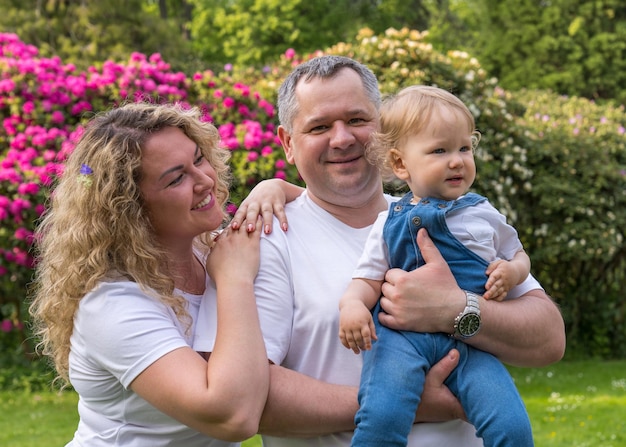 Mom stands next to dad holding a small oneyearold child with blond hair in her arms Family