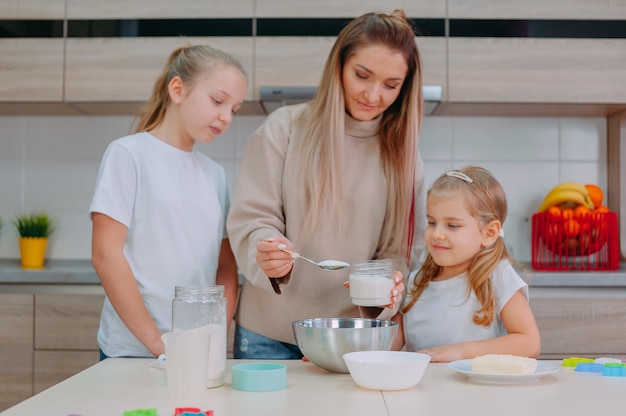 Mom teaches her daughters to cook dough in the kitchen.