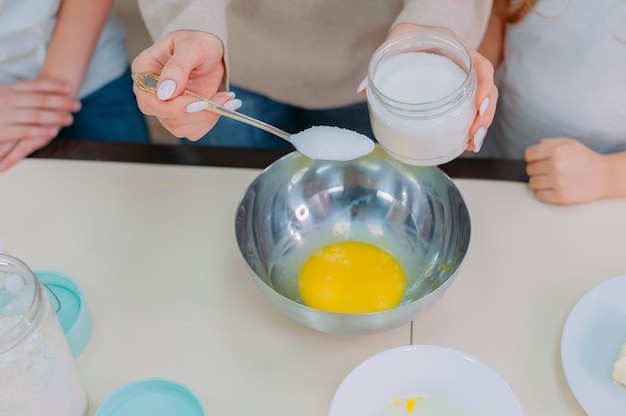 Mom teaches her daughters to make dough in the kitchen and beat eggs.