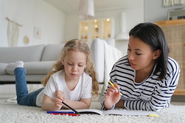 Mom teaches kid daughter to draw by colorful pencils lying on floor at home Children39s creativity