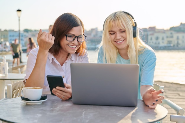 Mom and teenage daughter looking at laptop together sitting in an outdoor cafe