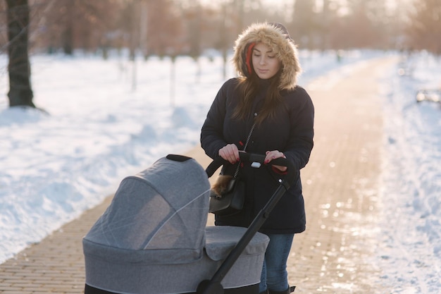 Mom walk with baby in pram winter park happy woman with her baby mom using phone in winter