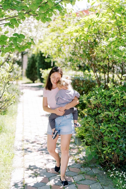 Mom walks along a path in the garden hugging a little girl in her arms