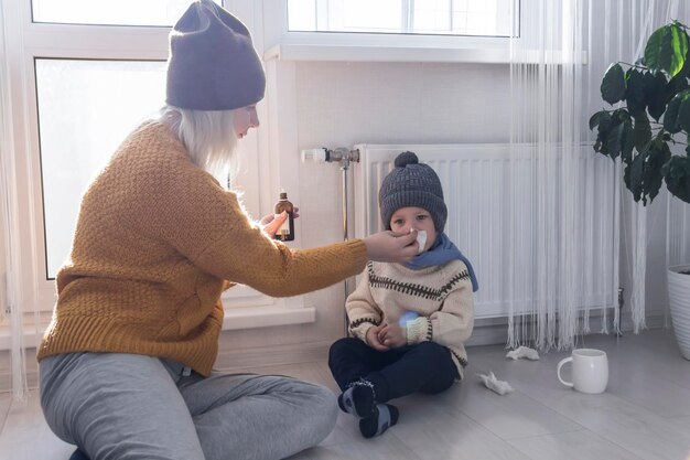 Mom wipes the snot of her little child with medicine in her hand near the heater