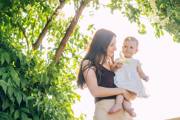 Mom with a baby in her arms on a sunny day walks through the park.