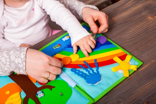 Mom with baby outlines the colors of the rainbow in a colored book of felt material handmade