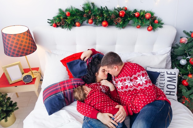 mom with a little boy sleeping on the bed and dad lying next to them bedroom with Christmas decorations family look