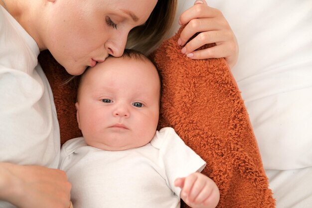 Mom with a newborn baby lies on the bed mother kisses the child mother's love