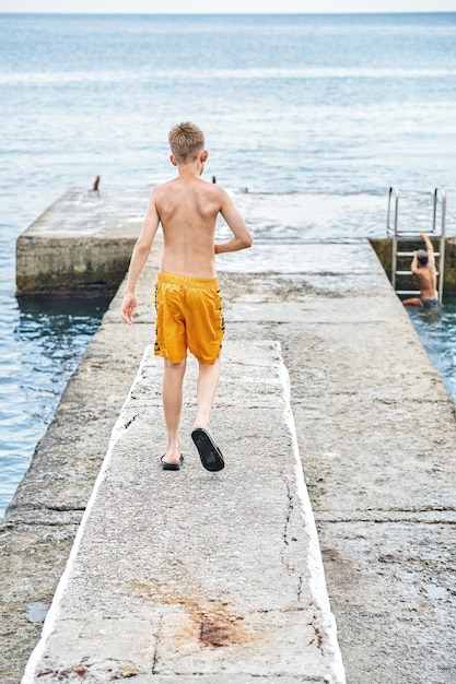 Moment of schoolboy walks on stone pier watching seascape