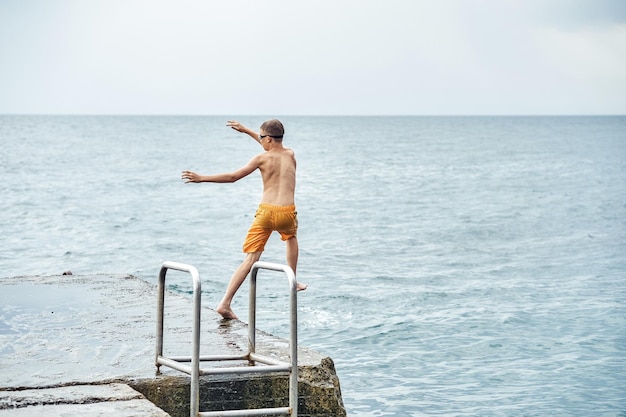 Moments of boy jumping from stone pier with ladder into sea doing tricks in combined image sequence