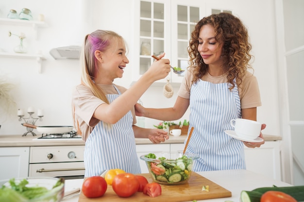 Mommy teaching her teen daughter to cook vegetable salad in kitchen