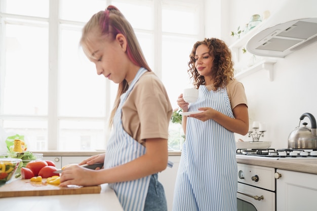 Mommy teaching her teen daughter to cook vegetable salad in kitchen