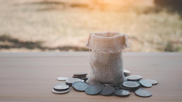 Money bag around by coin on the wooden table blur background