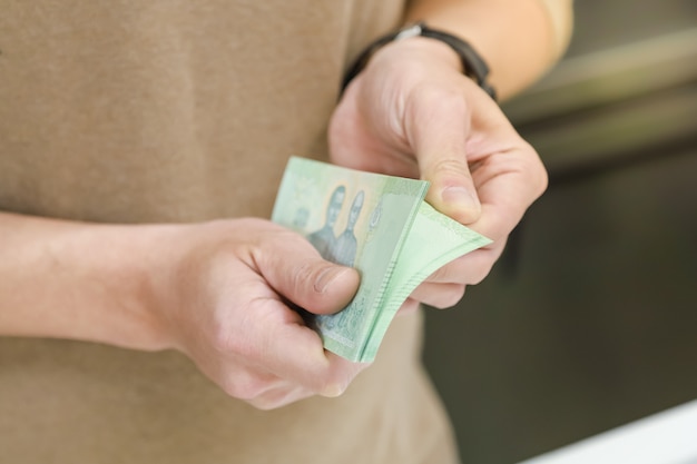 Money, Finance and saving concept. Close up of man hand holding and counting Thai Baht bank note.