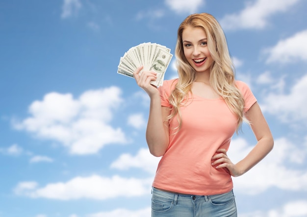 money, finances, investment, saving and people concept - happy young woman with dollar cash money over blue sky and clouds background