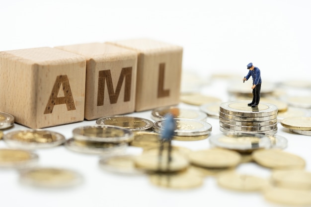 Money laundering concept. Miniature people, officer investigating pile of coins and wooden word block 