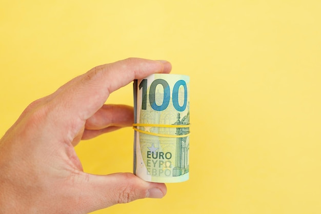 Money roll of euro banknotes yellow rubber band on yellow background