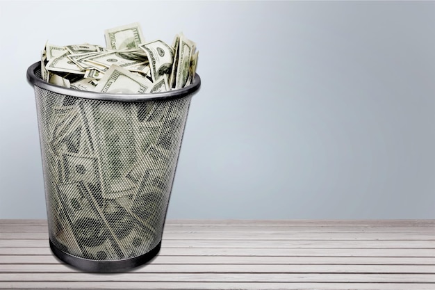 Money in trash bin on light background