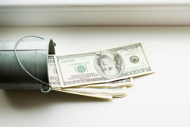 Moneybox, dollars in bucket on white window.light background