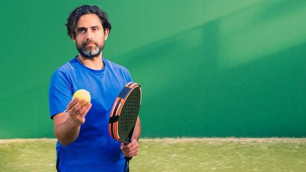 Monitor of padel holding black racket with yellow tennis ball in the hand