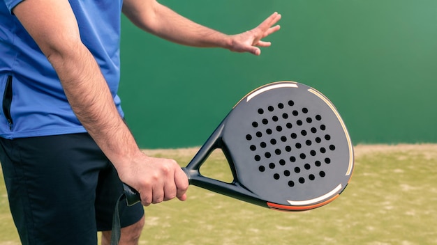 Monitor practicing paddle sport with a black padel racket on a green court grass