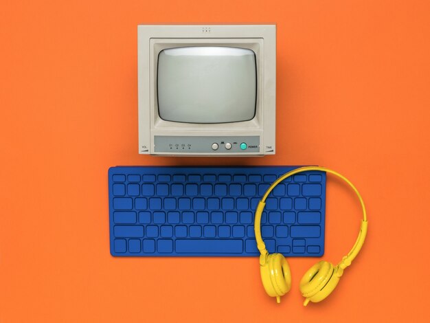 A monitor with a blue keyboard and yellow headphones on an orange background. Flat lay.