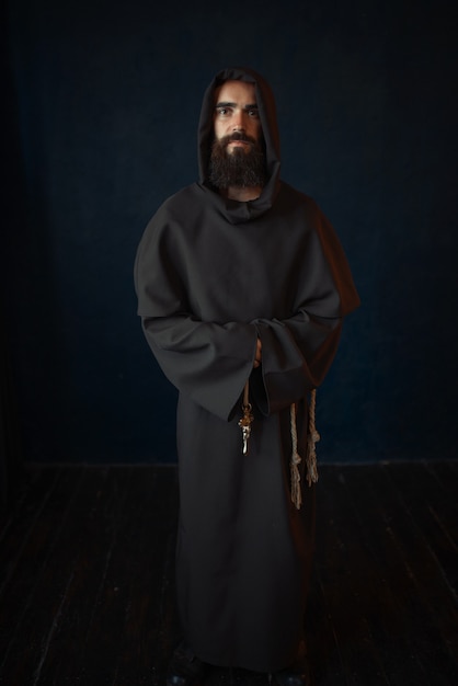 Monk in black robe with hood, religion. Mysterious friar in dark cape