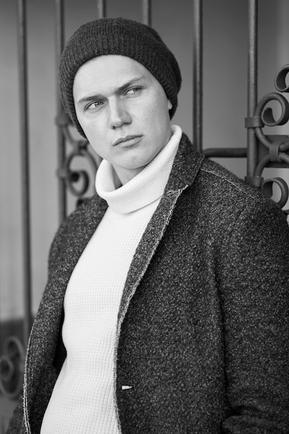 Monochrome portrait of fashionable stylish young attractive hipster trendy man wearing a coat, sweater and hat