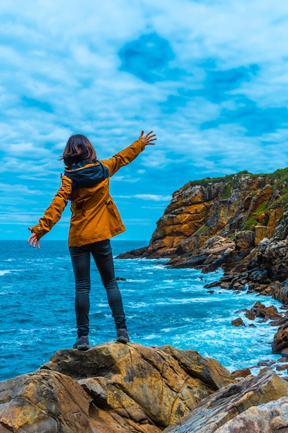 Monte Ulia in the city of San Sebastián, Basque Country. Visit the hidden cove of the city called Illurgita Senadia or Illurgita Senotia. A young woman in yellow jacket with open arms, vertical photo