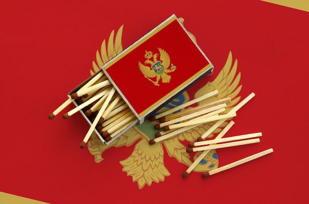 Montenegro flag  is shown on an open matchbox, from which several matches fall and lies on a large flag