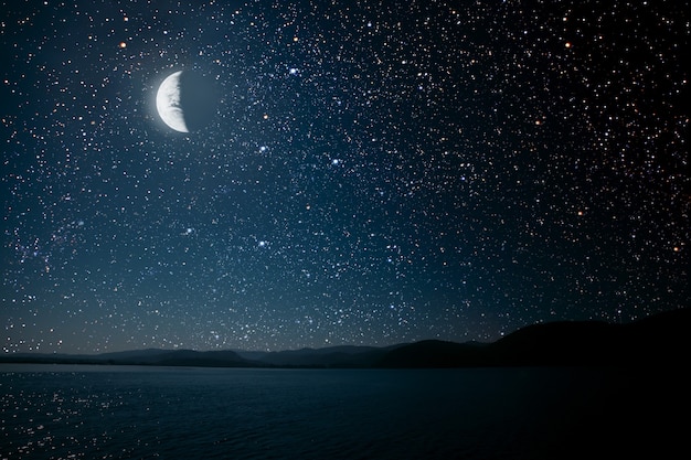 Moon against a bright night starry sky reflected in the sea.