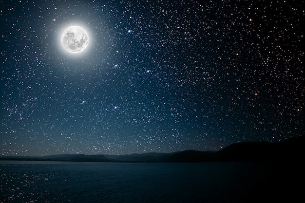 Moon against a bright night starry sky reflected in the sea.