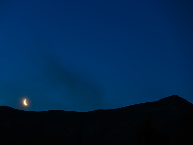 Moon in night sky over mountain ridge