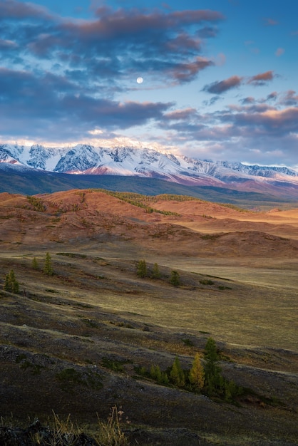 The moon over the North Chuysky ridge, dawn. Autumn in the Altai mountains. Russia