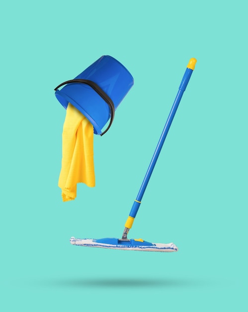 A mop and an overturned bucket with a yellow rag on a light background