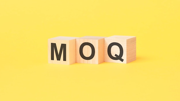 MOQ text on wood cubes yellow background business concept MOQ short for Minimum Order Quantity