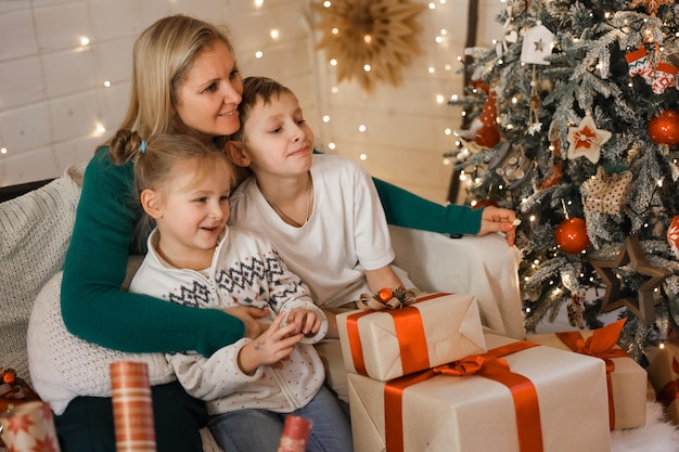 Morher and Kids in new year's Christmas atmosphere. Family are happy with Christmas and gifts. Children at the New Year tree with gifts.