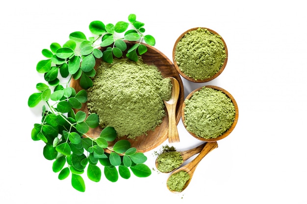 Moringa powder (Moringa Oleifera) in wooden bowl with original fresh Moringa leaves isolated