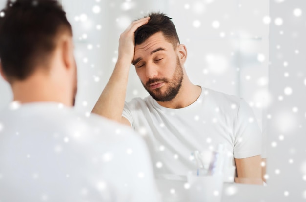 morning, awakening, hangover and people concept - sleepy young man in front of mirror at bathroom over snow