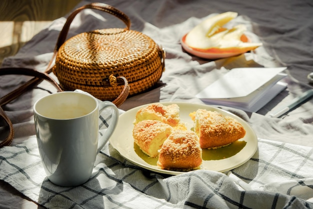 Morning breakfast in bed on blanket with tea fruit and pie wicker bag and notebook light green color