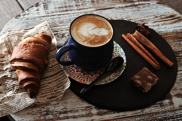 Morning Breakfast at cafe cappuccino in a mug, croissant, cinnamon