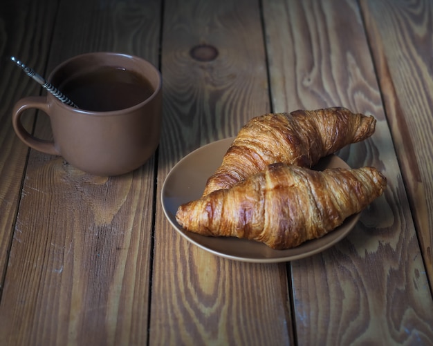 Photo morning breakfast at home. coffee with two croissants in a brown ceramic bowl on a simple wooden table