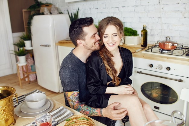 Morning Breakfast loving couple in the kitchen. A man and a woman hugging, cutting bread and cheese. Joy and smiles on the face of a loving couple