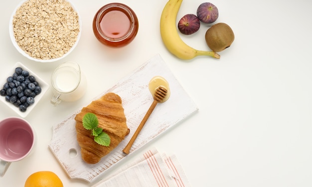 Morning breakfast, raw oatmeal flakes in a ceramic plate, milk in a decanter, blueberries and honey in a jar on a white table, top view, copy space