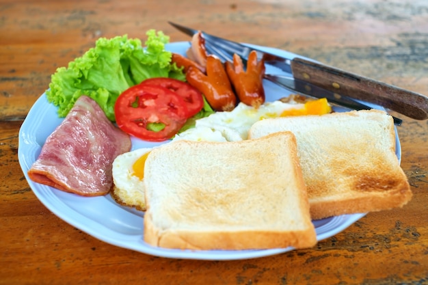 Morning breakfast with sausage, bacon, eggs and toast on wooden table