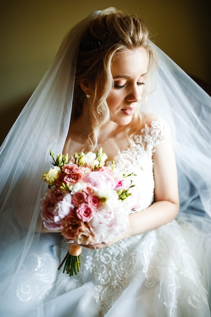 Morning of the bride. Beautiful bride in white wedding dress with bridal bouquet at wedding morning.