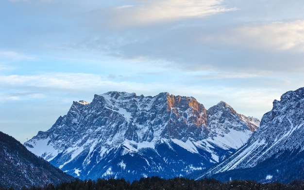 Morning cloudy sky and winter rock peak with forest on slope Austria.